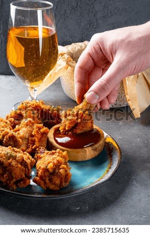 Cropped hand dipping fried chicken wing to bbq souse close up vertical photo. High quality photo