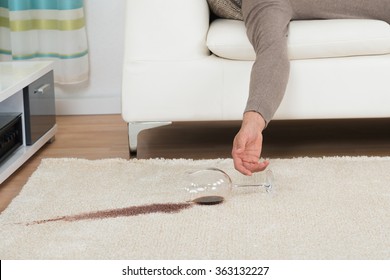 Cropped hand of drunk man spilling red wine on rug at home