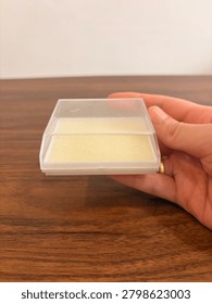 Cropped hand holding a small empty square plastic jewelry box with a transparent lid and white foam.