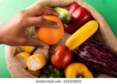 Cropped Hand Of Mixed Race Man Holding Fresh Orange Fruit Over Vegetables In Burlap Sack. Unaltered, Food, Healthy Eating, Organic Concept.