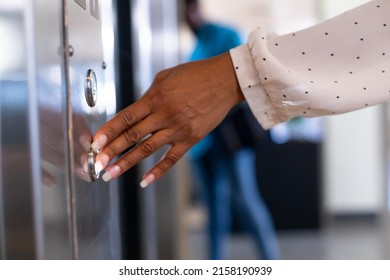 Cropped hand of young biracial businesswoman pressing elevator button at modern workplace. unaltered, business, modern office, convenience and technology concept.