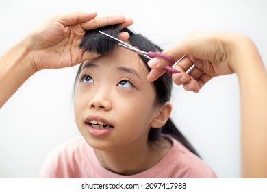 Cropped Hands Of Asian Mother Cutting Hair Of Her Young Daughter At Home. Lockdown Haircut At Home, During The Covid Pandemic.