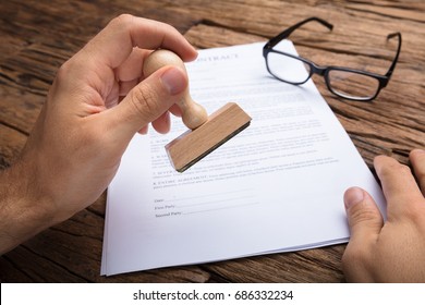 Cropped hands of businessman stamping contract paper at wooden table