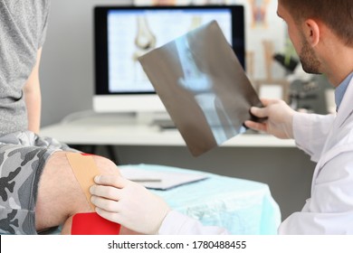 Cropped Head Of Doctor Looking At Photo Of Patient Injured Knee For Diagnosis And Treatment