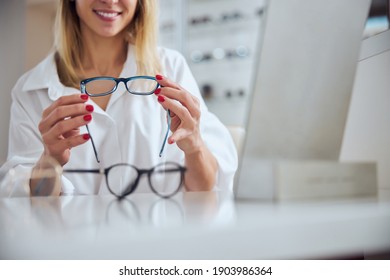 Cropped Head Portrait Of Pretty Lady In White Shirt Sitting At The Desk While Holding Eyeglasses Above The Table In Optician Center