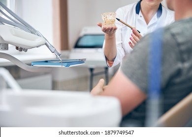 Cropped Head Of Woman Holding Jaw Model While Talking With Man In Dental Chair In Office