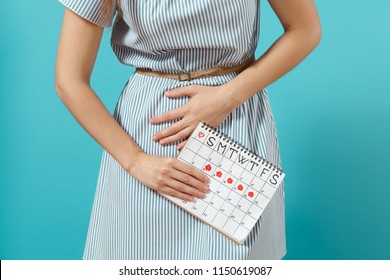 Cropped illness woman in blue dress holding periods calendar for checking menstruation days put hand on abdomen isolated on blue background. Medical, healthcare, gynecological concept. Copy space