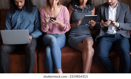 Cropped image addicted to modern technology four young diverse mixed race people sitting on sofa, involved in using different gadgets, spending time online in social networks, remote job concept. - Powered by Shutterstock