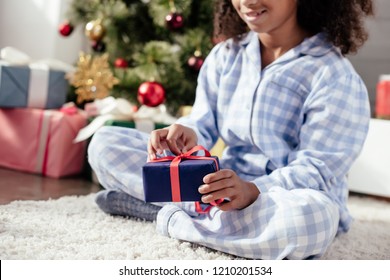 Cropped Image Of African American Child In Pajamas Opening Christmas Gift At Home