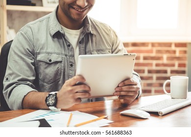 Cropped image of attractive Afro American businessman using a digital tablet and smiling while sitting in his office