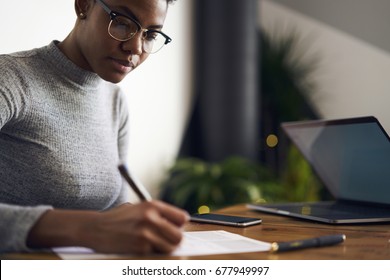 Cropped image of attractive afro american businesswoman signing contract for increase company income making notes on paper for proofreading details sitting near blurred copy space area for advertising
