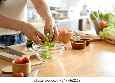 A cropped image of an attractive Asian woman making her healthy salad bowl in the kitchen, putting some lettuces in a bowl. home cooking, healthy and wellness lifestyle, domestic life - Powered by Shutterstock