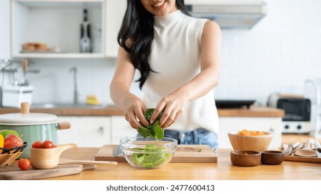 A cropped image of an attractive Asian woman making her healthy salad bowl in the kitchen, putting some lettuces in a bowl. home cooking, healthy and wellness lifestyle, domestic life - Powered by Shutterstock