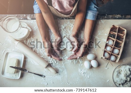 Cropped image of attractive young woman and her little cute daughter are cooking on kitchen. Having fun together while making cakes and cookies. Top view of mom with daughter making dough heart.