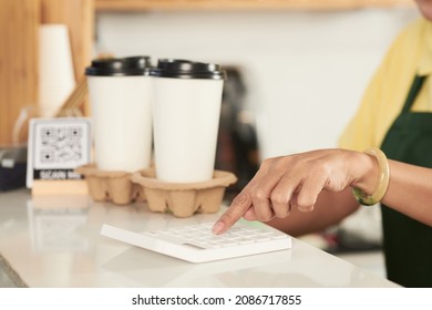Cropped image of barista with two take-out coffees on coffeeshop counter calculating price of order