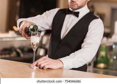 Cropped image of bartender pouring champagne into glass at bar counter