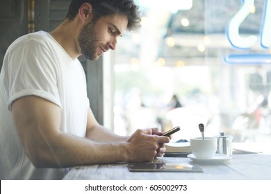 Cropped Image Bearded Hipster Guy Check Own Mail And Chatting With Friends In Social Networks On Mobile Phone Using Free Internet Sitting In Cafe Shop With Cup Of Coffee.  Advertising Copy Space Area