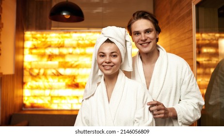 Cropped image of beautiful european couple looking at camera in spa salon. Young man and woman wear bathrobes and wrap bath towel on girl head. Rest with spa treatment. Leisure and spend time together