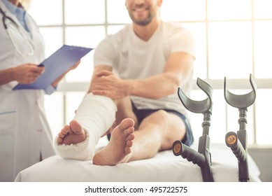 Cropped image of beautiful female medical doctor listening to handsome patient with broken leg and making notes while working in her office - Powered by Shutterstock