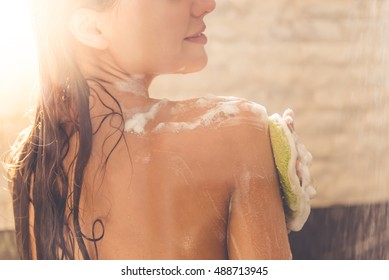 Cropped image of beautiful naked young woman smiling while taking shower in bathroom