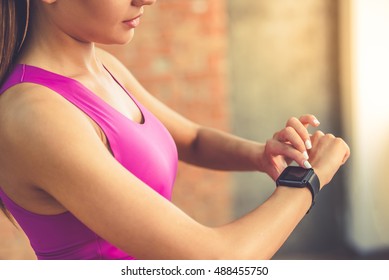 Cropped image of beautiful sports girl is switching on her fitbit before training while standing in fitness hall