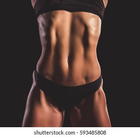 Cropped image of beautiful strong woman in black underwear showing her abdominal muscles, on dark background
