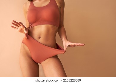 Cropped image of beautiful tanned young woman posing in comfortable underwear on beige background.Copy space.
