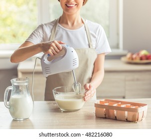 Cropped Image Of Beautiful Woman In Apron Smiling While Mixing Liquid Dough For Baking Using An Electric Mixer