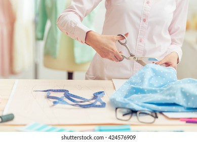 Cropped image of beautiful young designer cutting cloth using scissors while working in dressmaking salon