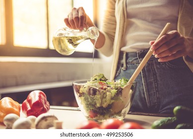 Cropped image of beautiful young girl mixing salad while cooking in kitchen at home