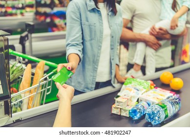 Cropped image of beautiful young parents and their little daughter standing near cash desk in the supermarket. Mom is giving a credit card - Powered by Shutterstock