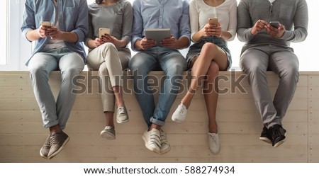 Cropped image of beautiful young people in casual clothes using gadgets while sitting together on the window sill
