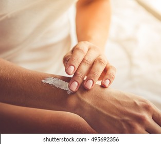 Cropped image of beautiful young woman applying hand cream while sitting on bed at home