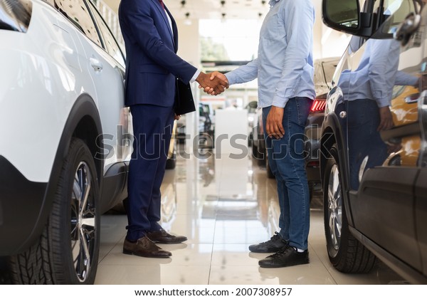 Cropped Image Of Black Car Seller Shaking Hands With\
Client After Successful Deal, Unrecognizable Salesman Selling Auto\
To Customer In Modern Dealership Center, Handshaking After\
Agreement, Side View