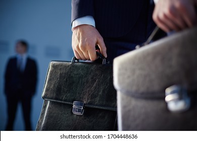 Cropped image of business partners carrying briefcases on the foreground while their colleague standing on the background