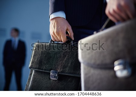 Cropped image of business partners carrying briefcases on the foreground while their colleague standing on the background