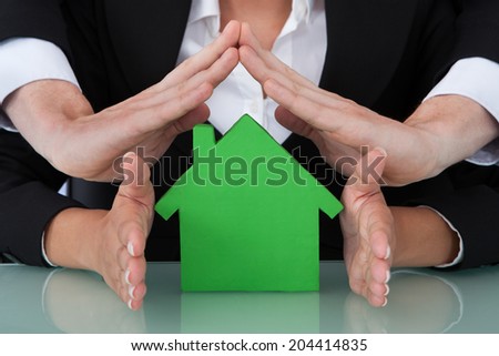 Cropped image of business people sheltering green house model in office