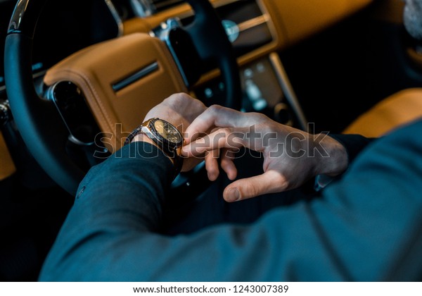 cropped\
image of businessman checking watch in luxury\
car