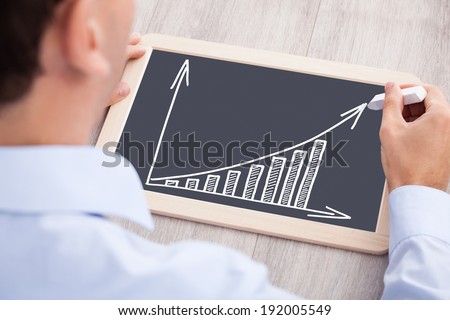 Cropped image of businessman drawing bargraph on slate at desk in office