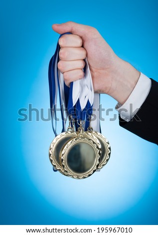 Cropped image of businessman holding medals over blue background