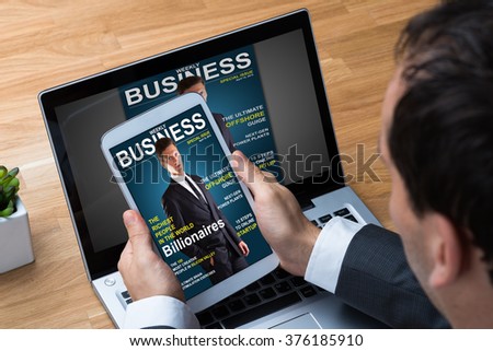 Cropped image of businessman reading business magazine on tablet and laptop in office
