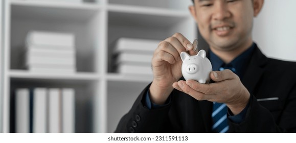 Cropped image of businessman standing holding piggy bank and putting coins into it The concept of saving money, investing, financial planning. cost savings. - Shutterstock ID 2311591113
