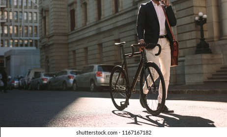 Cropped image of businessman walking on city street with a bicycle and talking on mobile phone. Man in formal wear going to work with cycle using phone. - Powered by Shutterstock