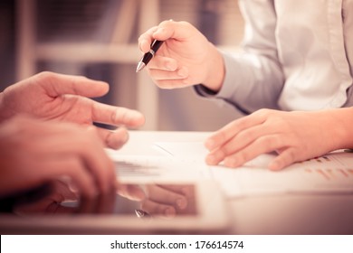 Cropped image of a businesswoman holding a pen and pointing at something while dealing with her colleague on the foreground  - Powered by Shutterstock