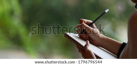 Cropped image of a businesswoman's hand is taking notes while standing over the office glass wall.