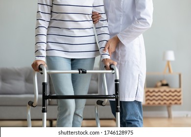 Cropped image caregiver helping to disabled aged female patient walk with walker physical therapist teach her, supporting during exercise therapy. Nursing at home, aftercare and physiotherapy concept