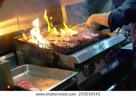 Cropped image of chef grilling steaks in commercial kitchen