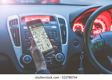 Cropped image. Closeup of smartphone in hand of girl sitting behind the wheel of modern car. Young woman uses digital gadget. She paves way to browser. On screen of smartphone map of area