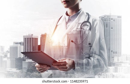 Cropped image of confident medical industry employee standing outdoors and holding tablet in hands. Young female doctor using tablet. Double exposure