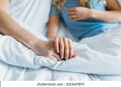 Cropped Image Of Couple Holding Hands In Bed